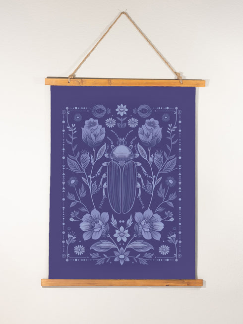 A symmetrical wall tapestry in monochromatic navy blue featuring a detailed scarab beetle surrounded by flowers and botanical elements, mounted on a wooden dowel with natural twine.